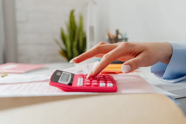 A close-up image of a person's hand using a red calculator on a desk with paperwork. Bookkeeping foundations mistakes, and the fixes that hold